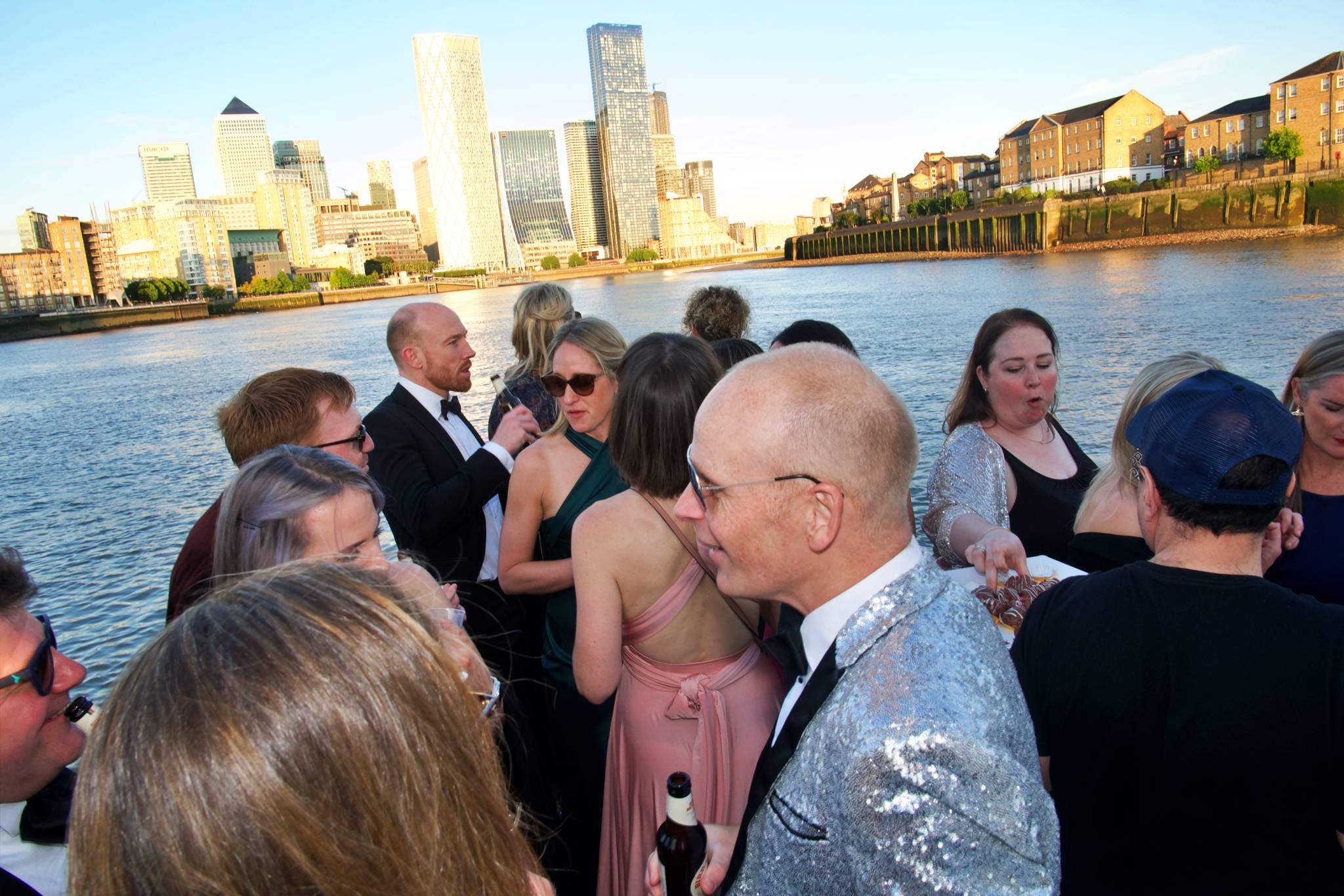 Guests networking on the deck of a London party boat with the skyline behind